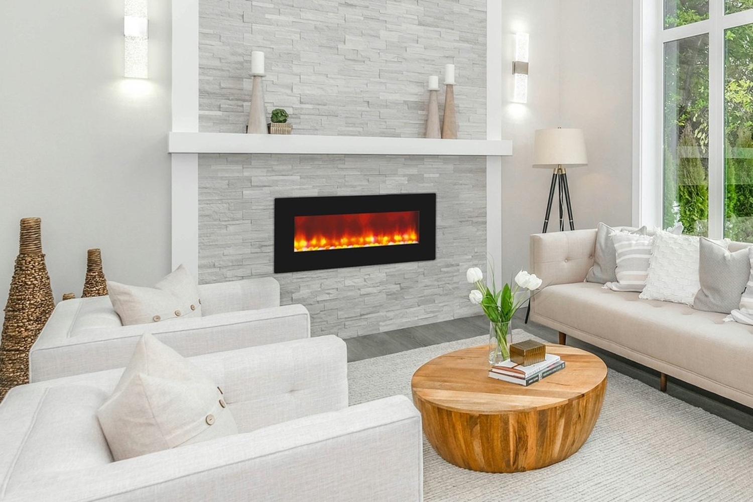 Woonkamer met open haard, witte banken, houten tafel en groot raam met groen.