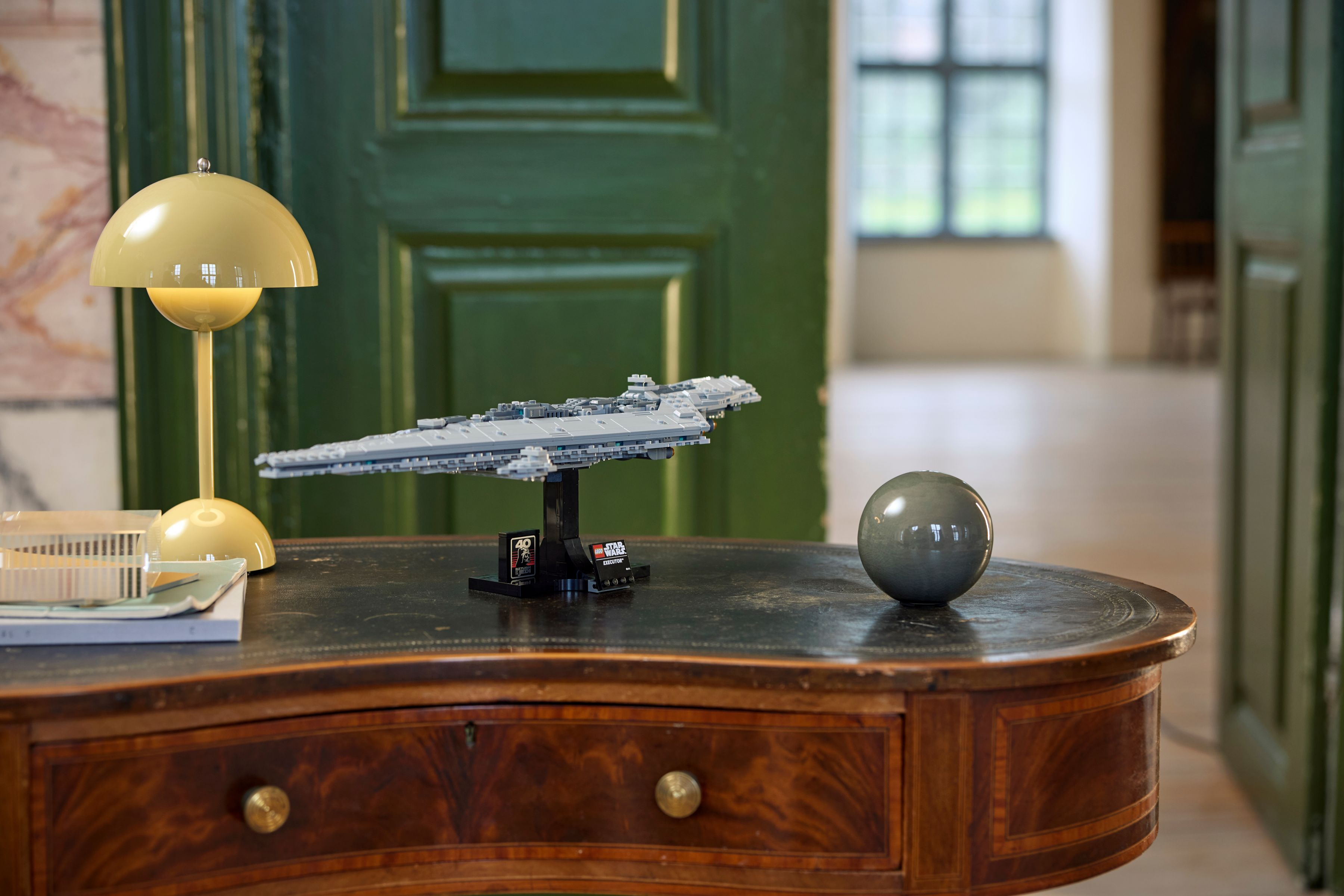 Una nave Lego di Star Wars è su un tavolo con una lampada e una sfera grigia. Porta verde sullo sfondo.