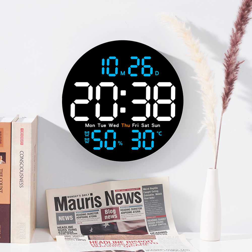 Un orologio digitale mostra data e ora. Sotto, un giornale e un vaso con piante. Libri a sinistra.