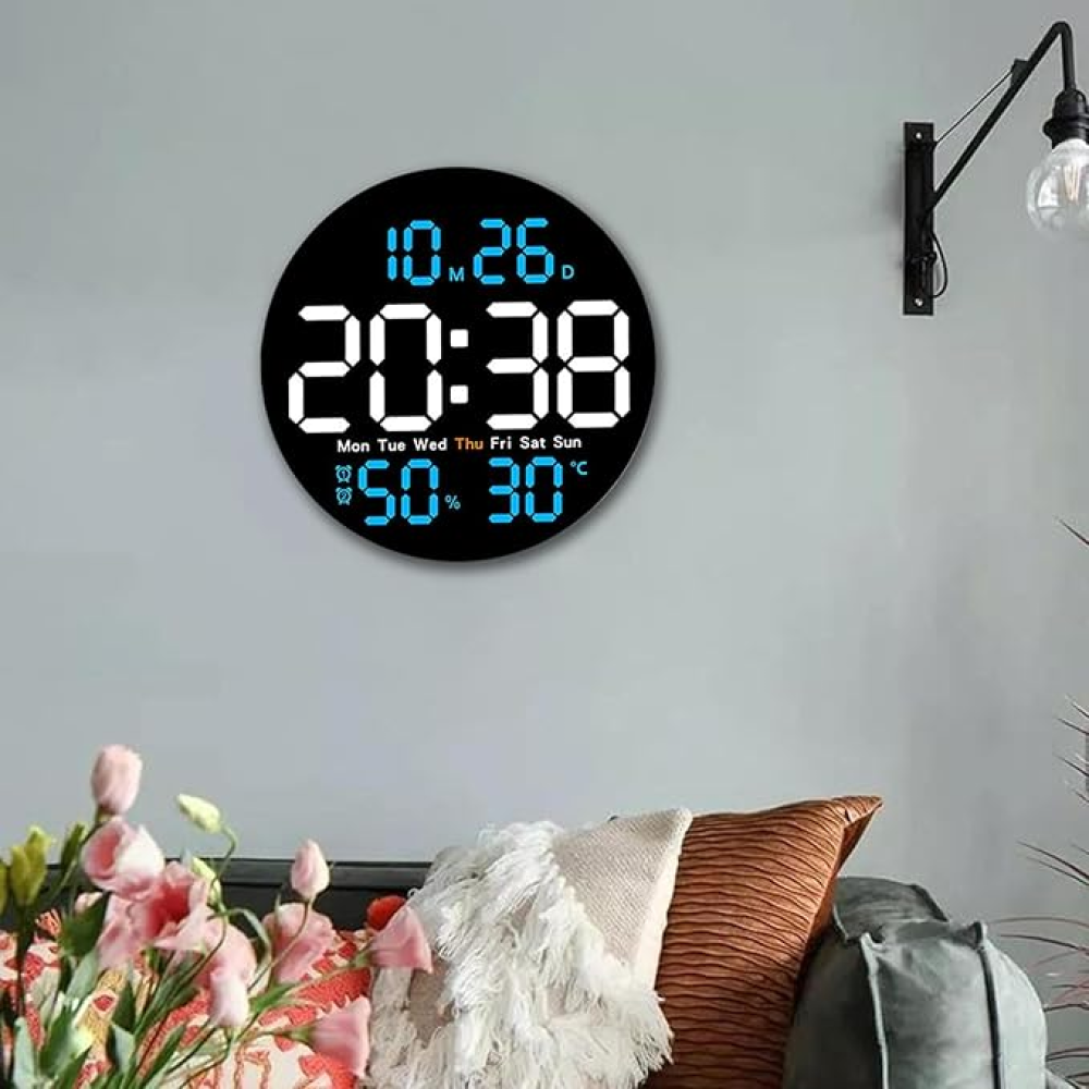 Un orologio digitale su una parete grigia mostra ora, data, umidità e temperatura. Sotto, un divano con cuscini e fiori è visibile.