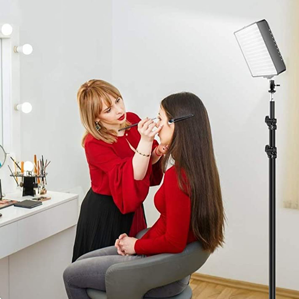 Una truccatrice applica il trucco a una cliente. Una luce intensa illumina la scena. Un mobile da trucco con lampadine è sullo sfondo.