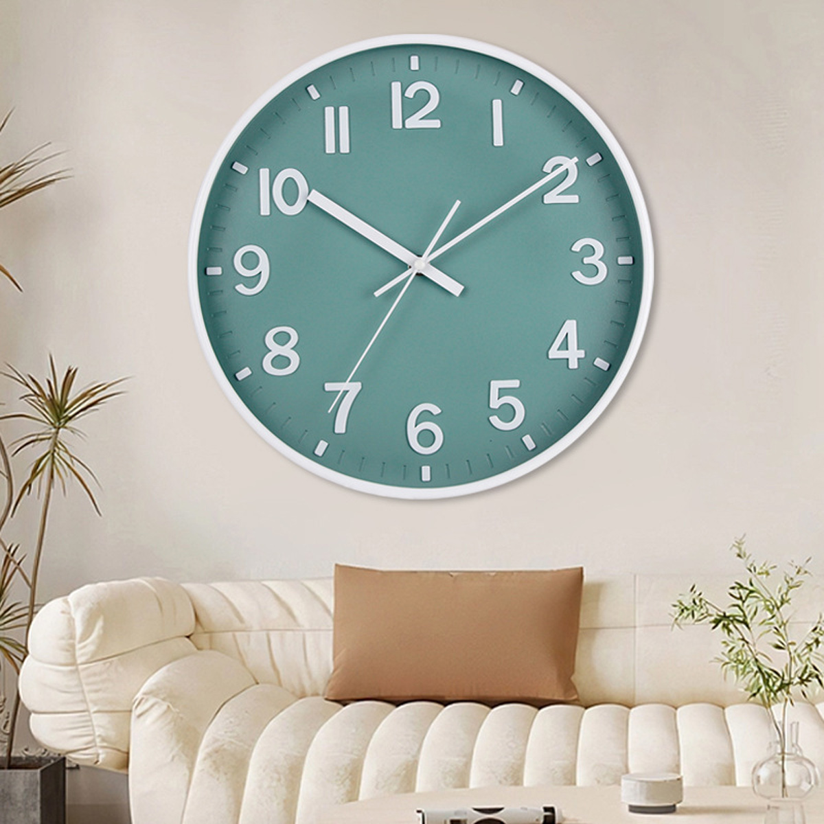 Un orologio da parete verde acqua con lancette e numeri bianchi è appeso sopra un divano beige con un cuscino marrone. Sono presenti anche piante e decorazioni.