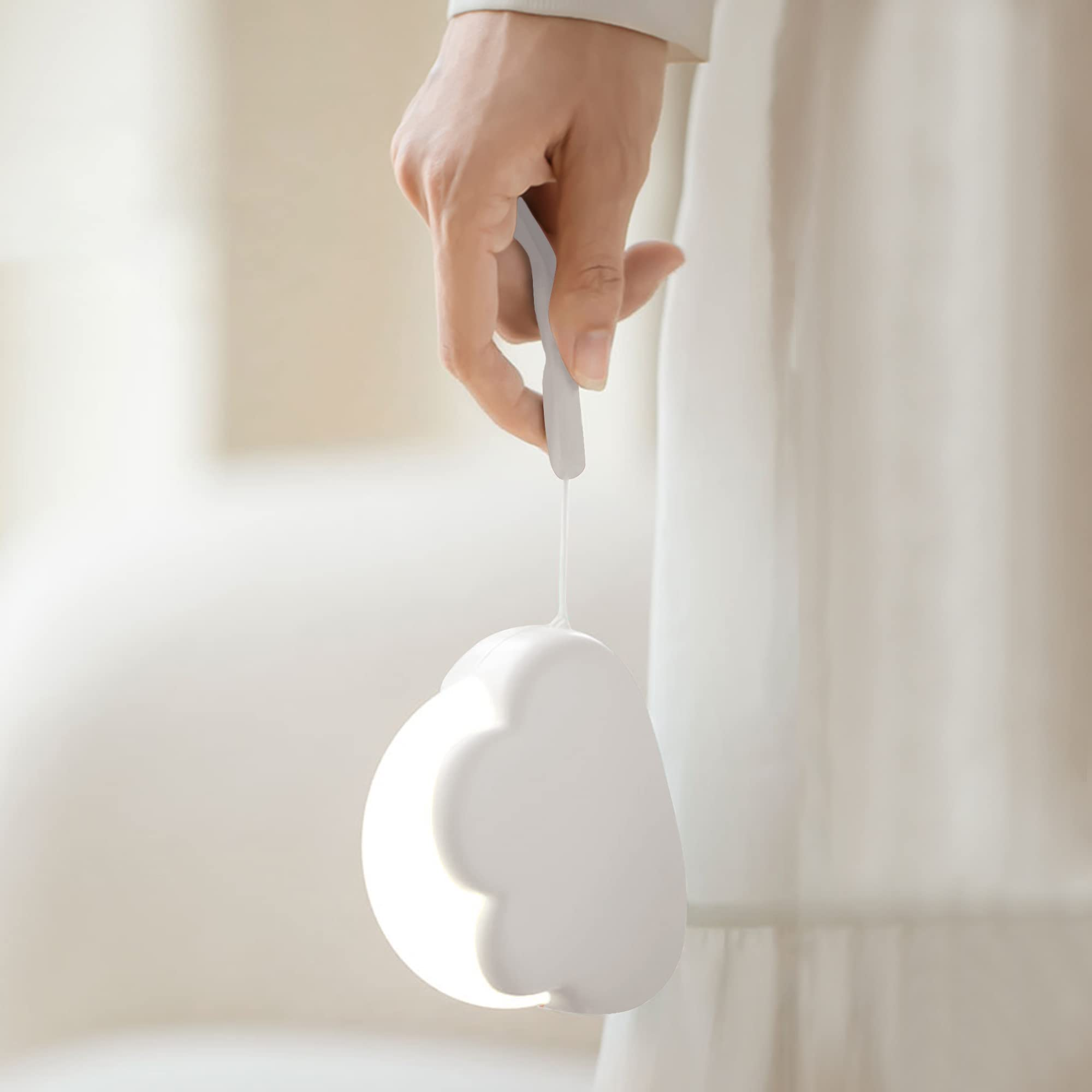 Una mano tiene in mano una lampada bianca a forma di nuvola. Lo sfondo è una tenda bianca.