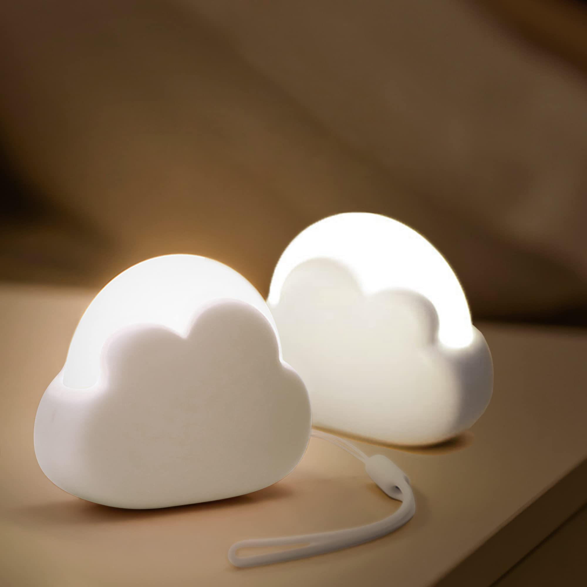 Due luci notturne a forma di nuvola, che brillano di bianco. Sono posizionate su una superficie marrone, con sfondo abbinato.