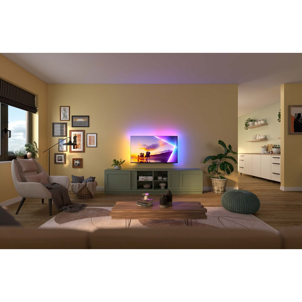 Scena di soggiorno con TV, divano, arte, piante e tavolino. Mostra uno spettacolo di luci colorate in TV. Tonalità calde.