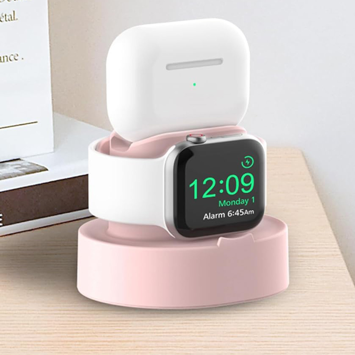 Ein rosa Ladeständer hält eine weiße Apple Watch, AirPods und eine Uhr mit der Anzeige 12:09. Der Hintergrund zeigt eine Holzoberfläche und Papier.
