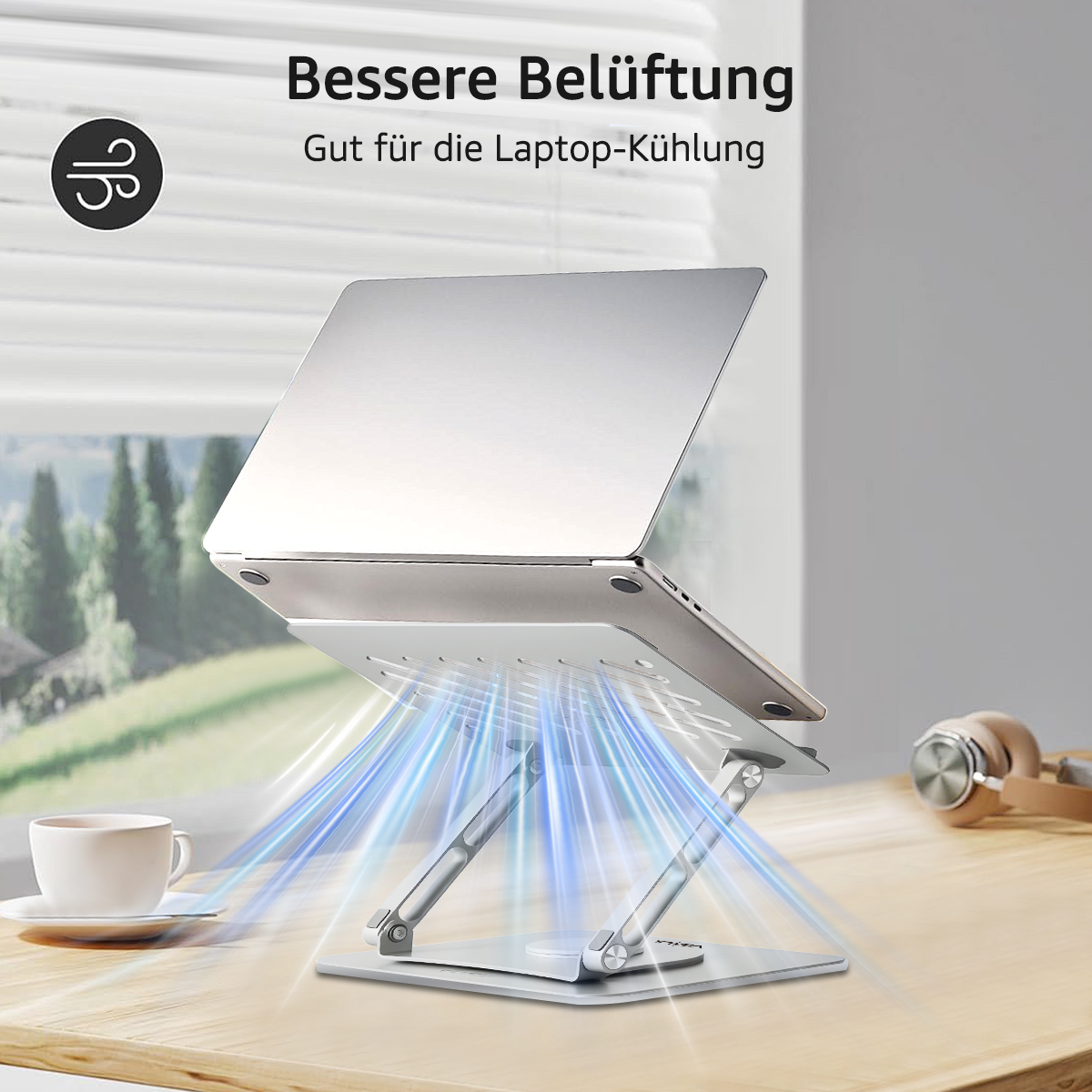 Laptop auf silbernem Ständer mit blauem Luftstrom. Kaffeetasse und Kopfhörer auf dem Holztisch, Fenster im Hintergrund.