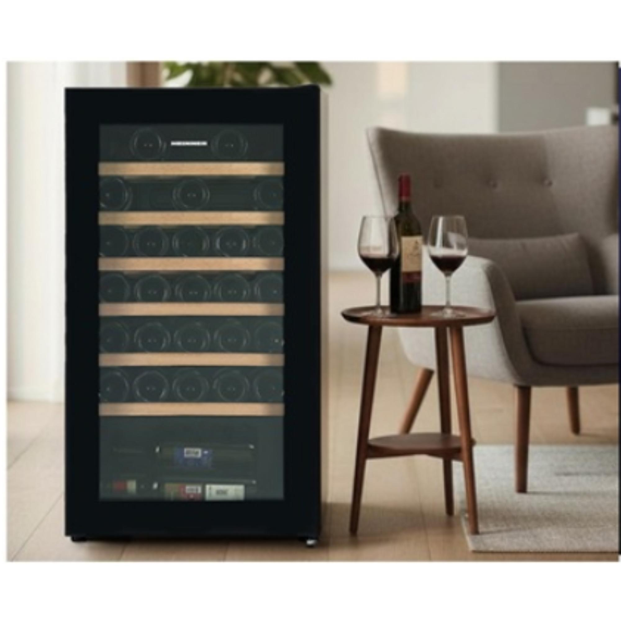A wine cooler with wine bottles. A table with wine and glasses, and a gray armchair in the background.