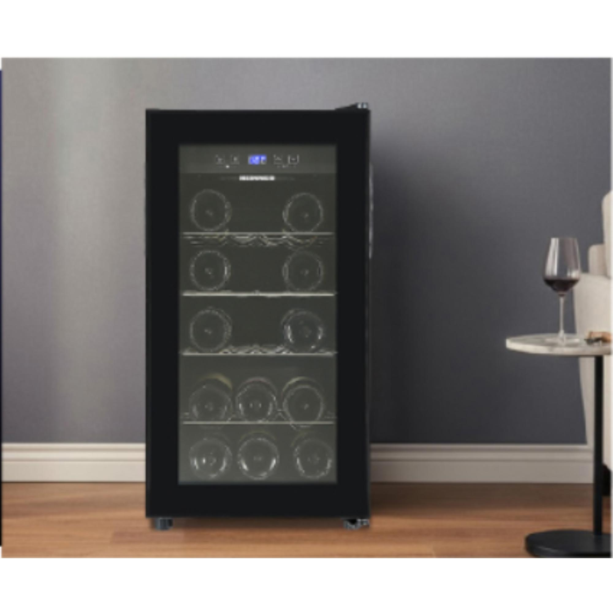 A black wine cooler with bottles is in a room. A table with a wine glass sits to the right. The wall is gray.