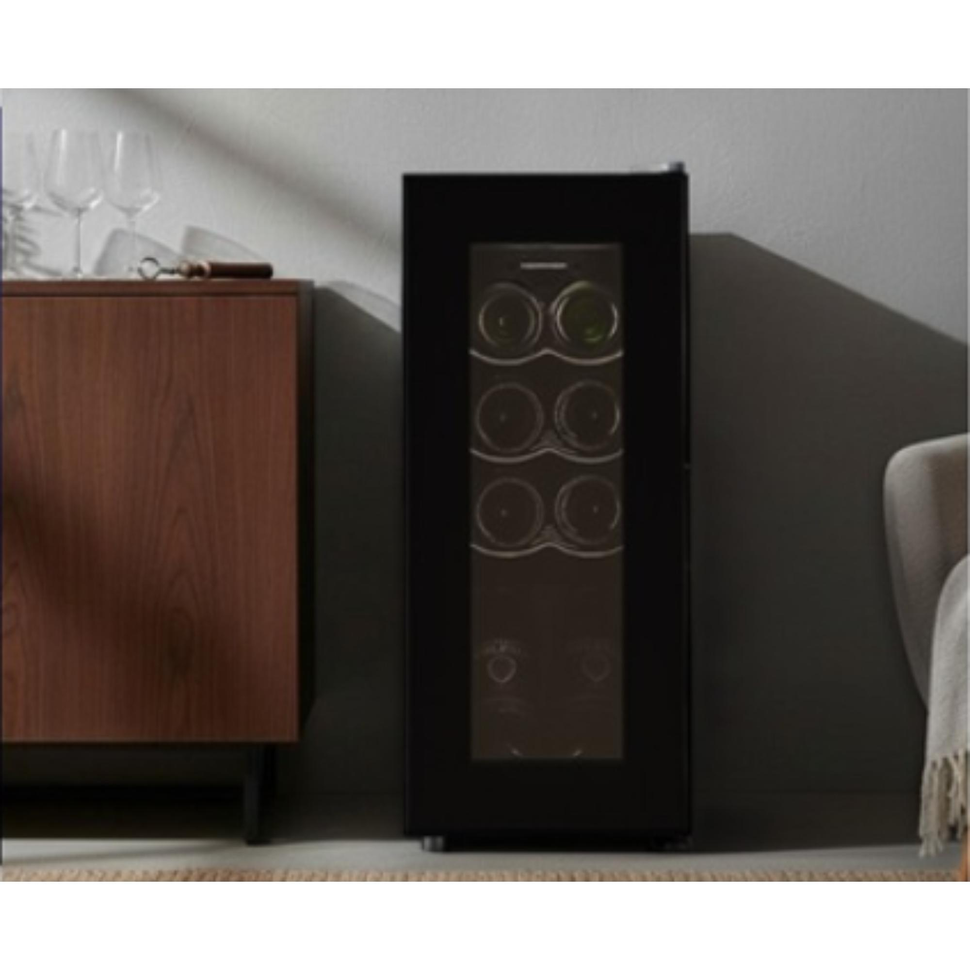 A black wine cooler with bottles inside. A wooden cabinet and wine glasses are to the left.