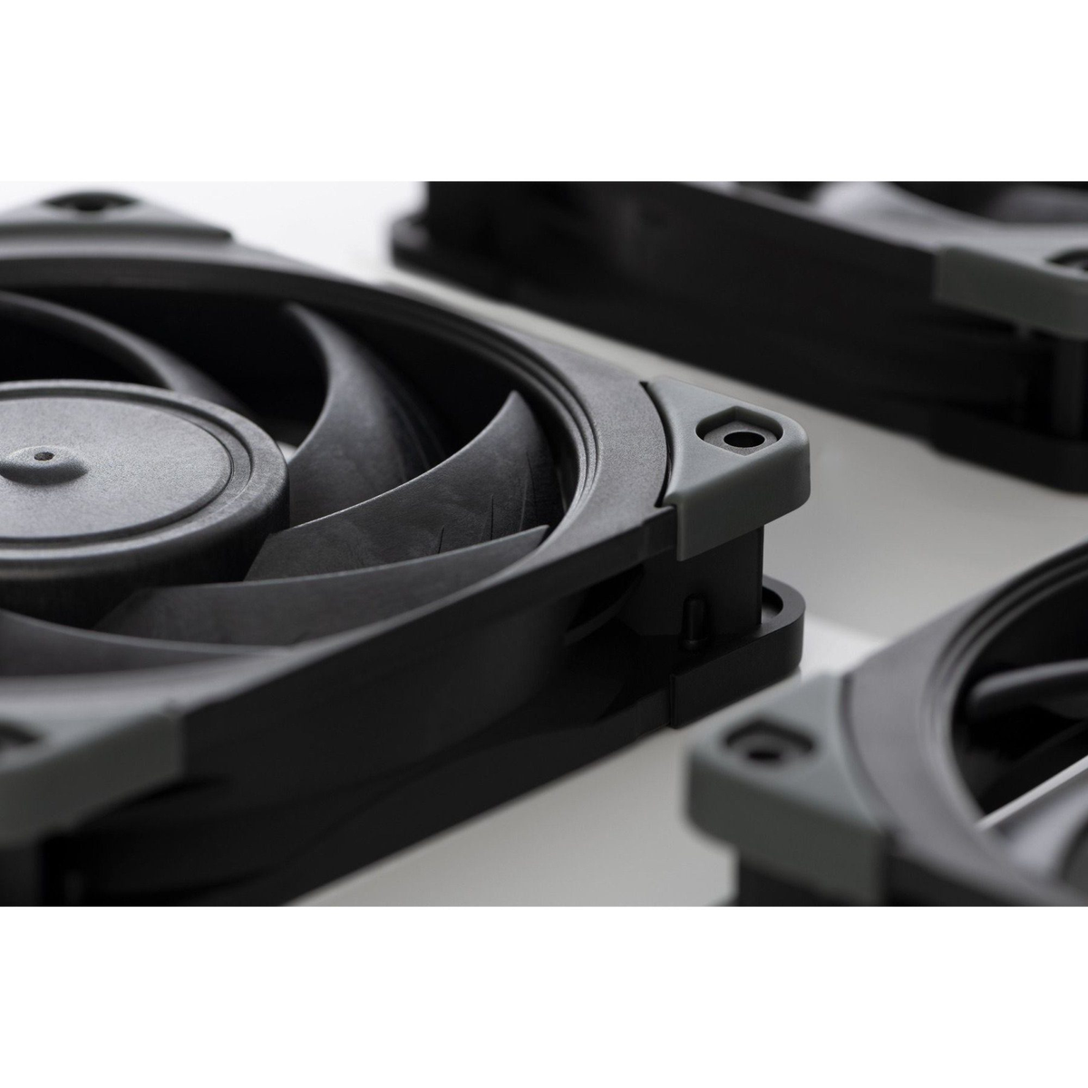 Zbliżenie czarnych wentylatorów komputerowych z szarymi akcentami, ułożonych na białej powierzchni. Widoczne są łopatki.