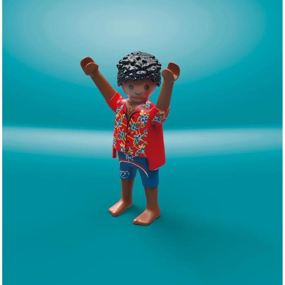 Una figura de Playmobil con camisa roja con estampados florales y pantalones cortos azules, con los brazos en alto. Sobre un fondo turquesa.
