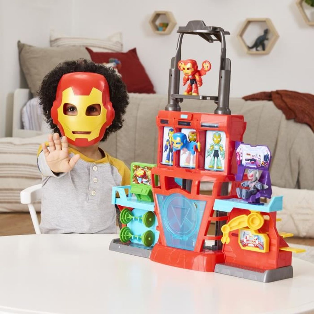 Un niño con una máscara de Iron Man y un juego de juguetes. El set tiene una base roja con figuras de superhéroes. Una mesa blanca está en primer plano.