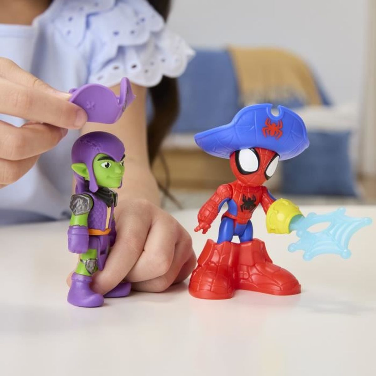 Dos figuras de juguete: Duende Verde y Spider-Man con sombrero de pirata y telaraña. El fondo muestra una cama.