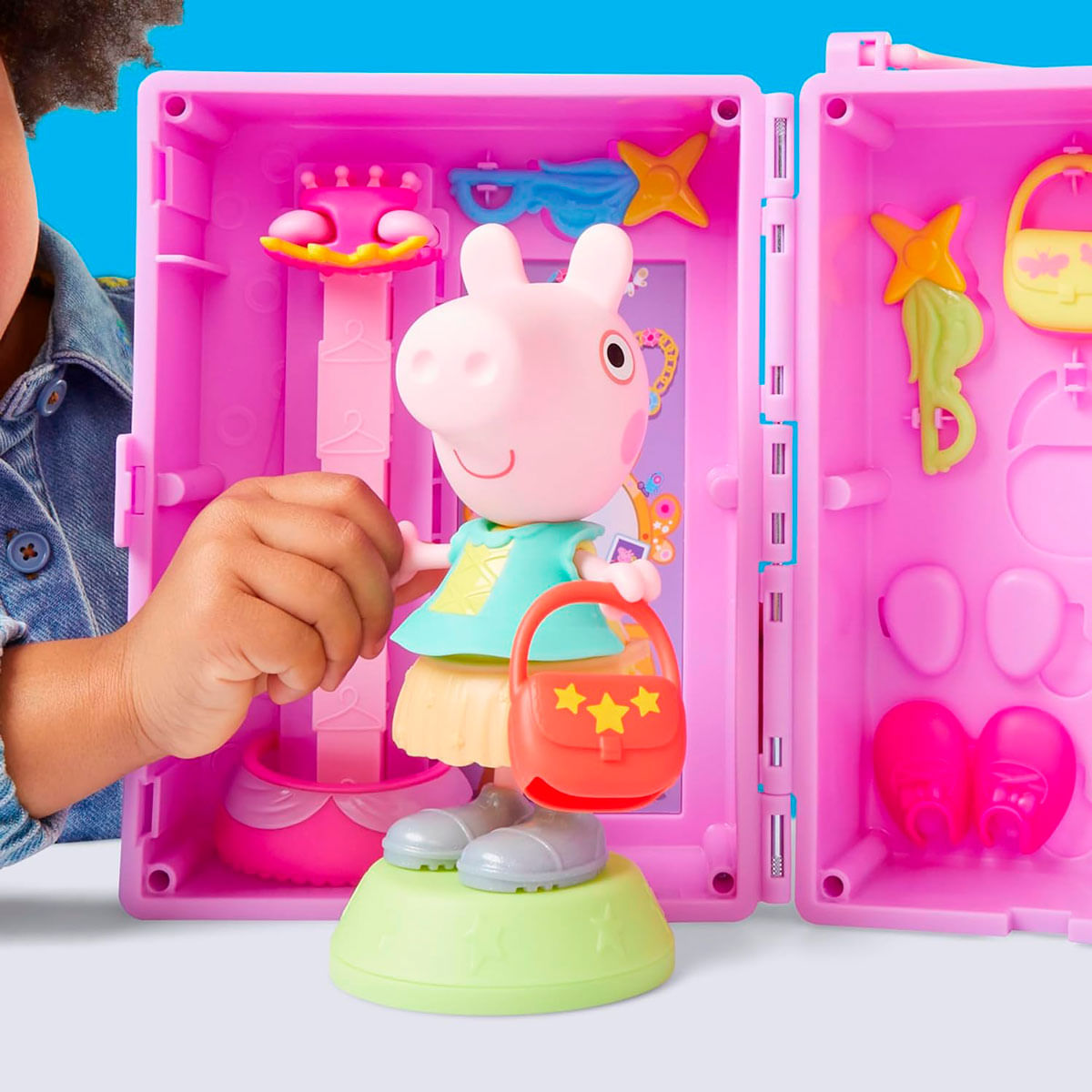 Juguete de Peppa Pig dentro de un estuche rosa, con accesorios. Se ve la mano de un niño. El juguete tiene un bolso rojo con estrellas amarillas.