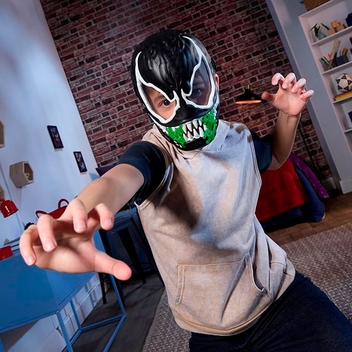 Un niño con una máscara de Venom, con dientes verdes y acentos blancos, posa amenazante. Una pared de ladrillos está al fondo.