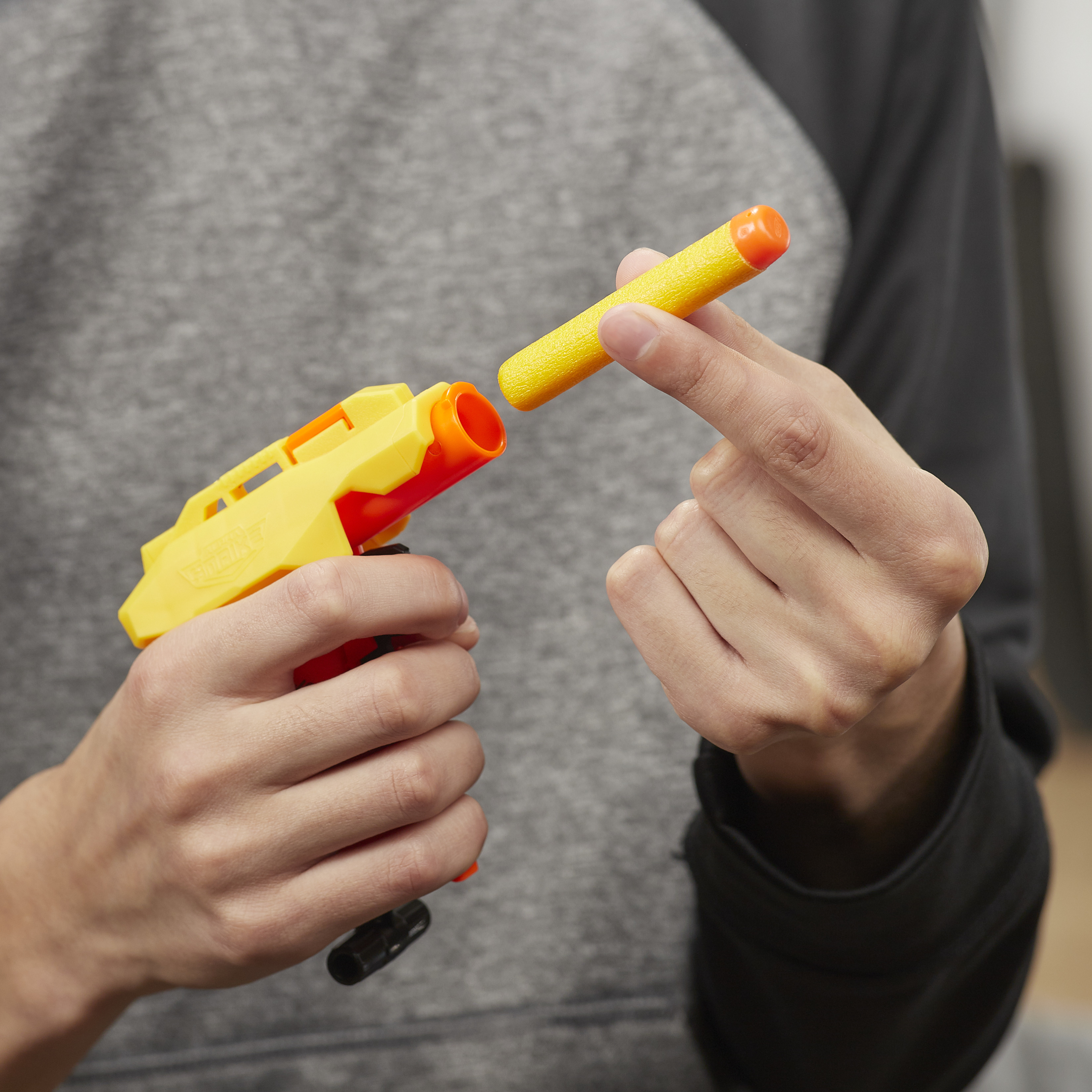 Una persona sostiene una pistola de juguete amarilla y un dardo naranja, preparándose para cargar el dardo en la pistola.