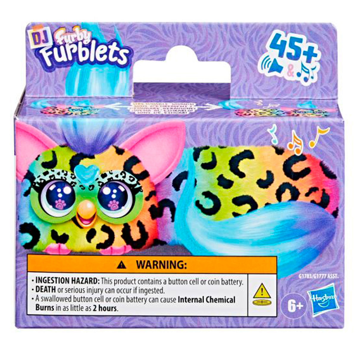 Una caja de Furby Furblets. Tiene un diseño animal colorido con una advertencia sobre peligros de ingestión. La caja es morada y blanca.