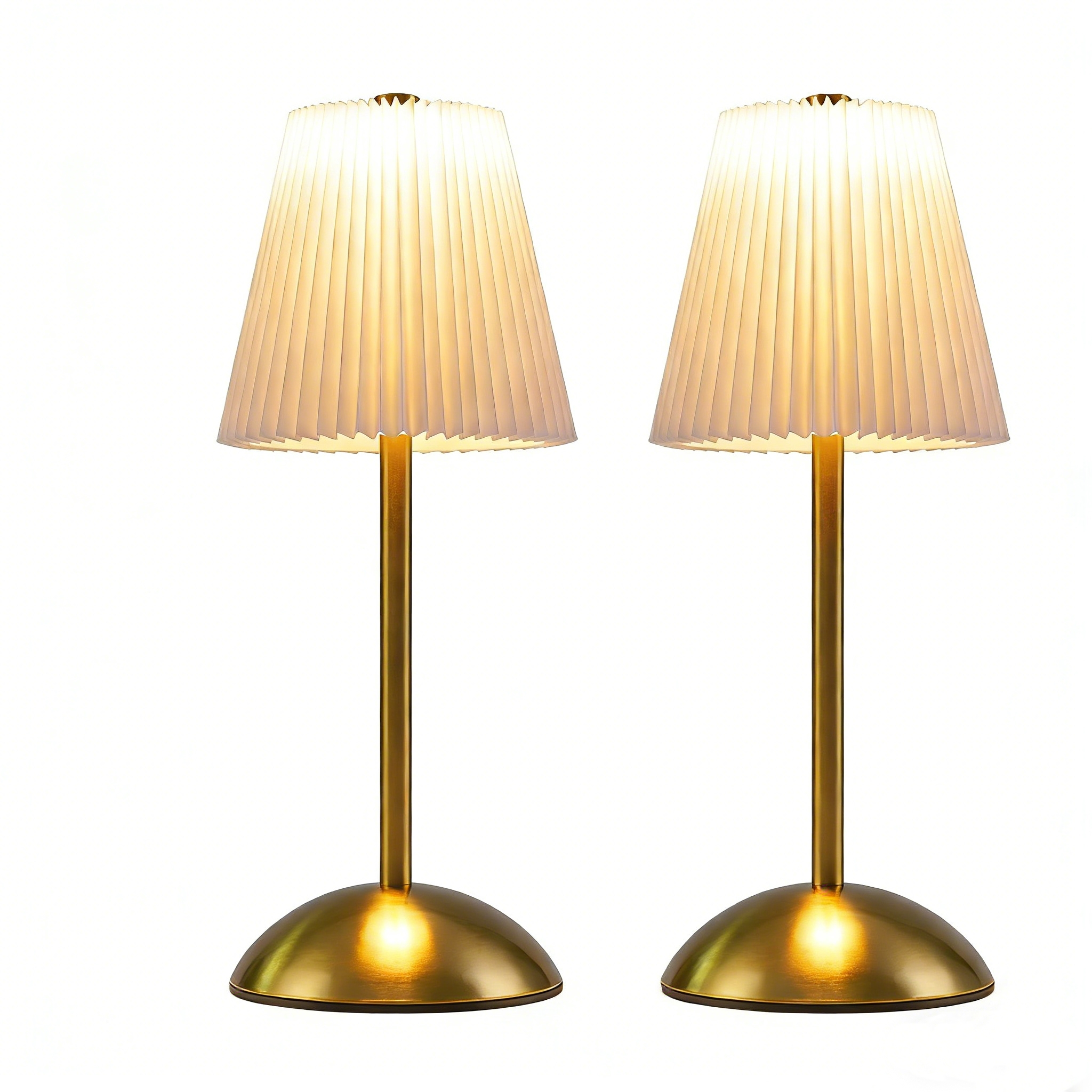 Due lampade da tavolo color oro con paralumi plissettati su sfondo bianco. I paralumi sono color crema e illuminati.