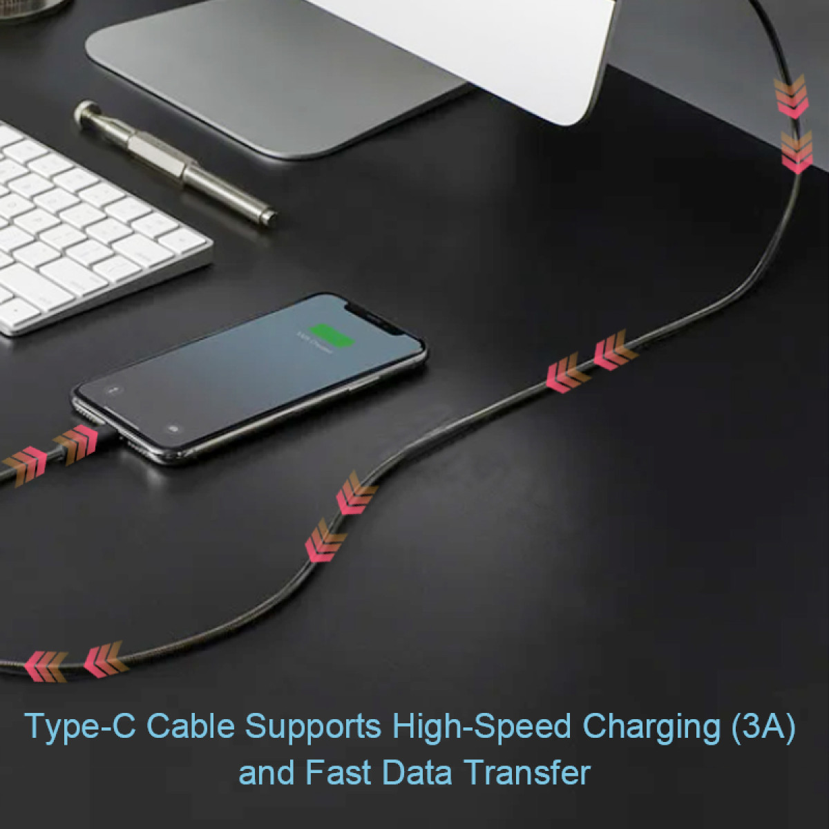 Telefon ładujący się kablem, na czarnym biurku. Klawiatura, monitor i długopis również widoczne w tle.