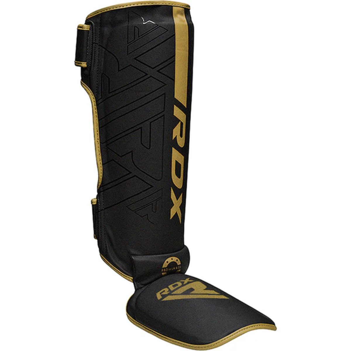 Ein schwarzer und goldener RDX-Schienbeinschutz. Der Schienbeinschutz hat einen goldenen Streifen, goldene Verzierungen und das RDX-Logo in Gold.