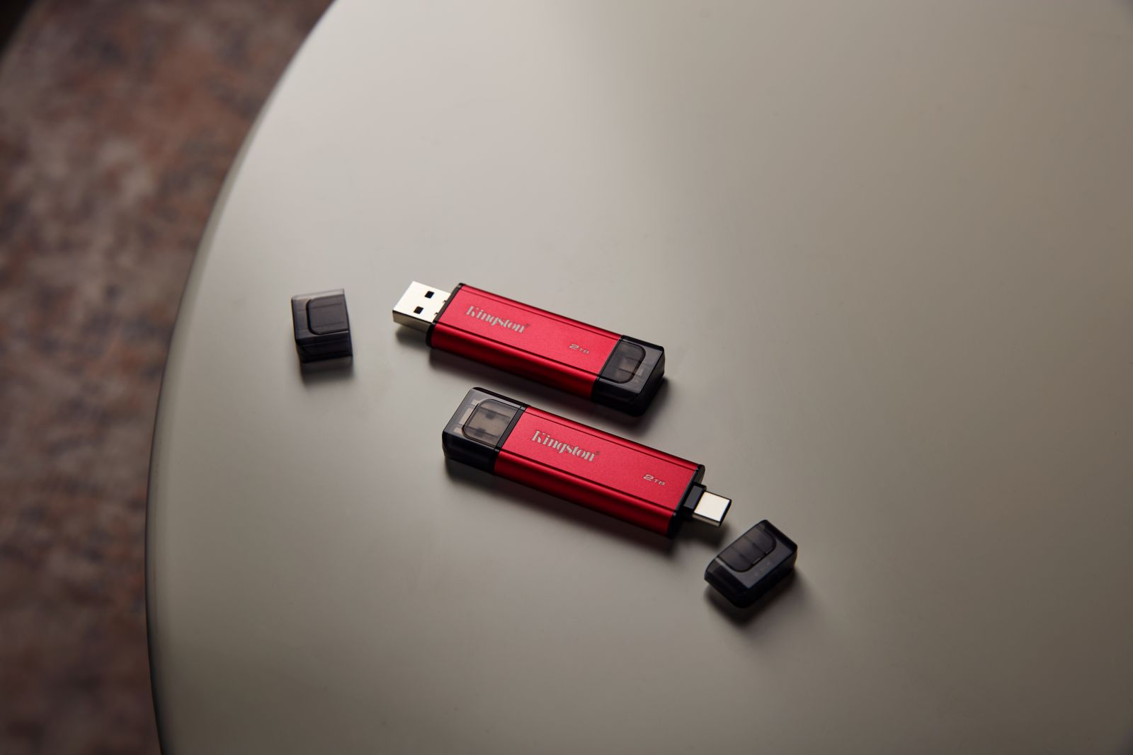 Zwei rote Kingston-USB-Laufwerke mit schwarzen Kappen auf grauer Oberfläche. Ein Laufwerk hat seine Kappe abgenommen.