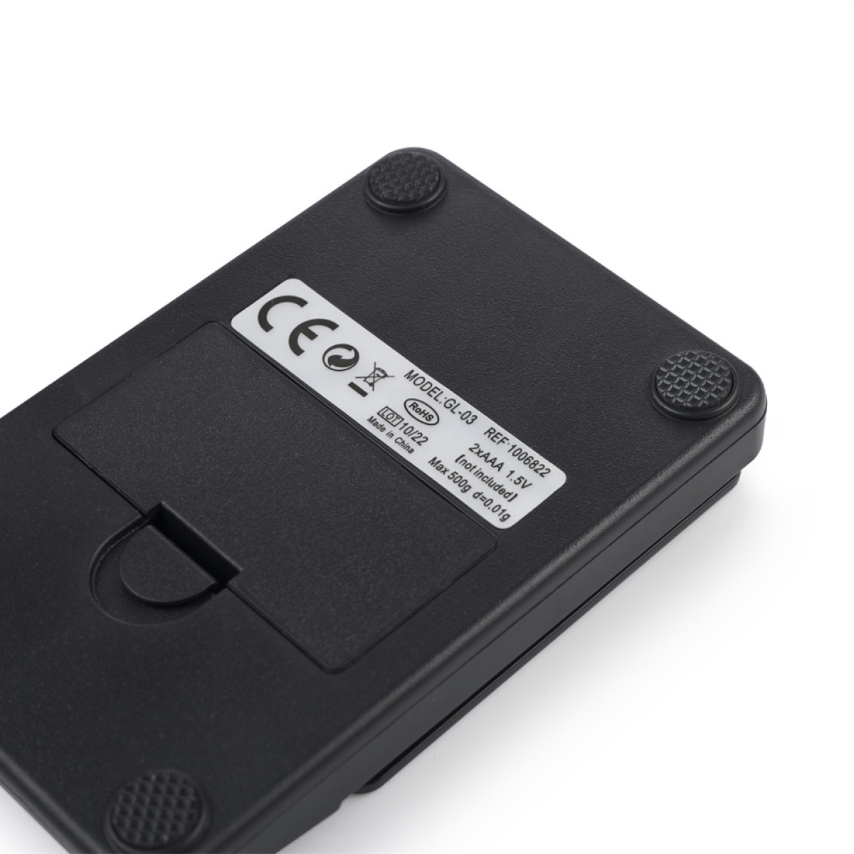 Zbliżenie spodu czarnej wagi. Ma gumowe nóżki, komorę baterii i naklejkę ze specyfikacjami. Białe tło.