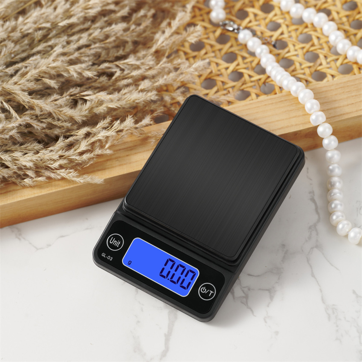 Czarna waga cyfrowa wyświetla 0,00. Obok kłosy pszenicy, drewniana taca i perłowy naszyjnik na białej powierzchni.