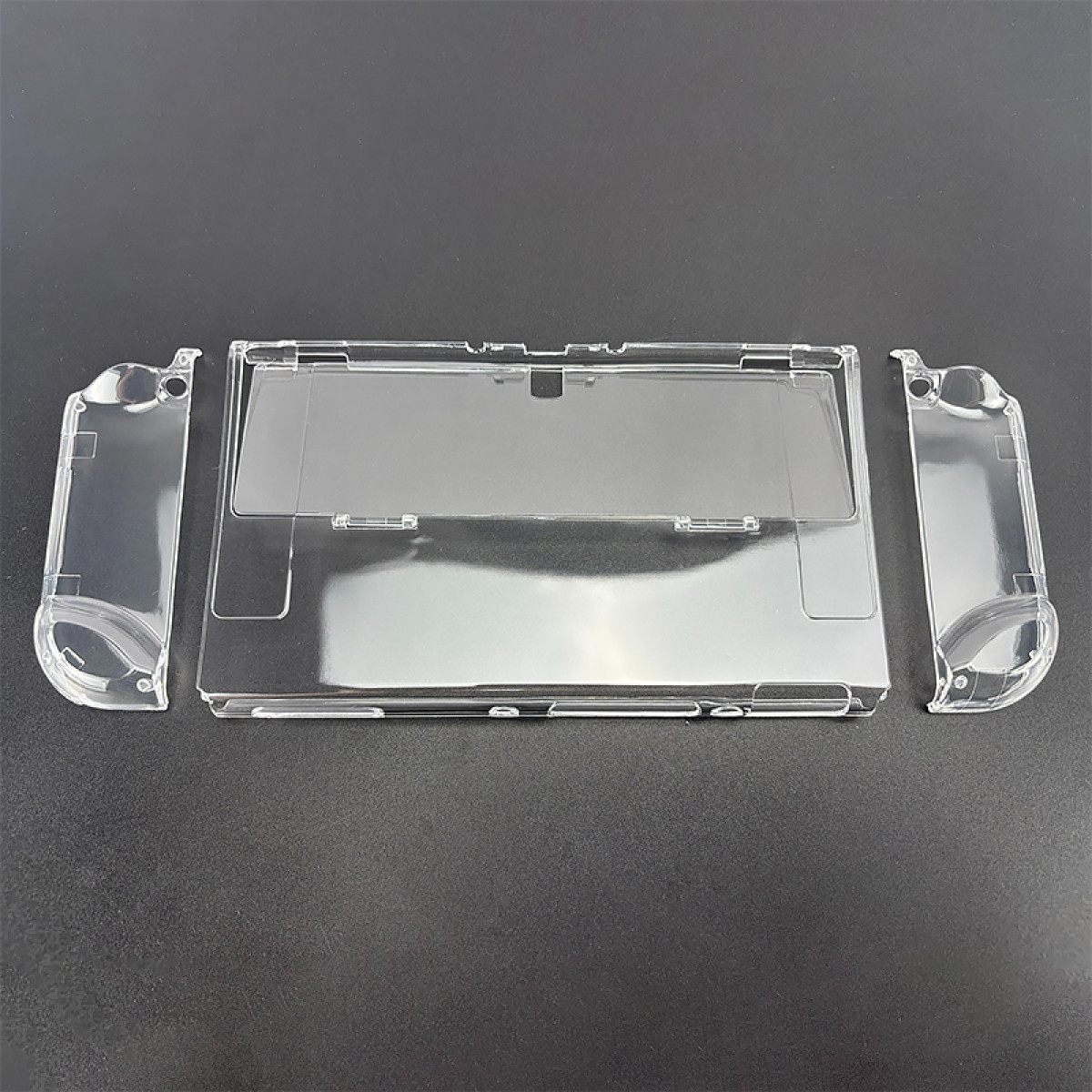 Pièces en plastique transparent pour Nintendo Switch: un couvercle principal et deux poignées latérales, sur surface gris foncé.