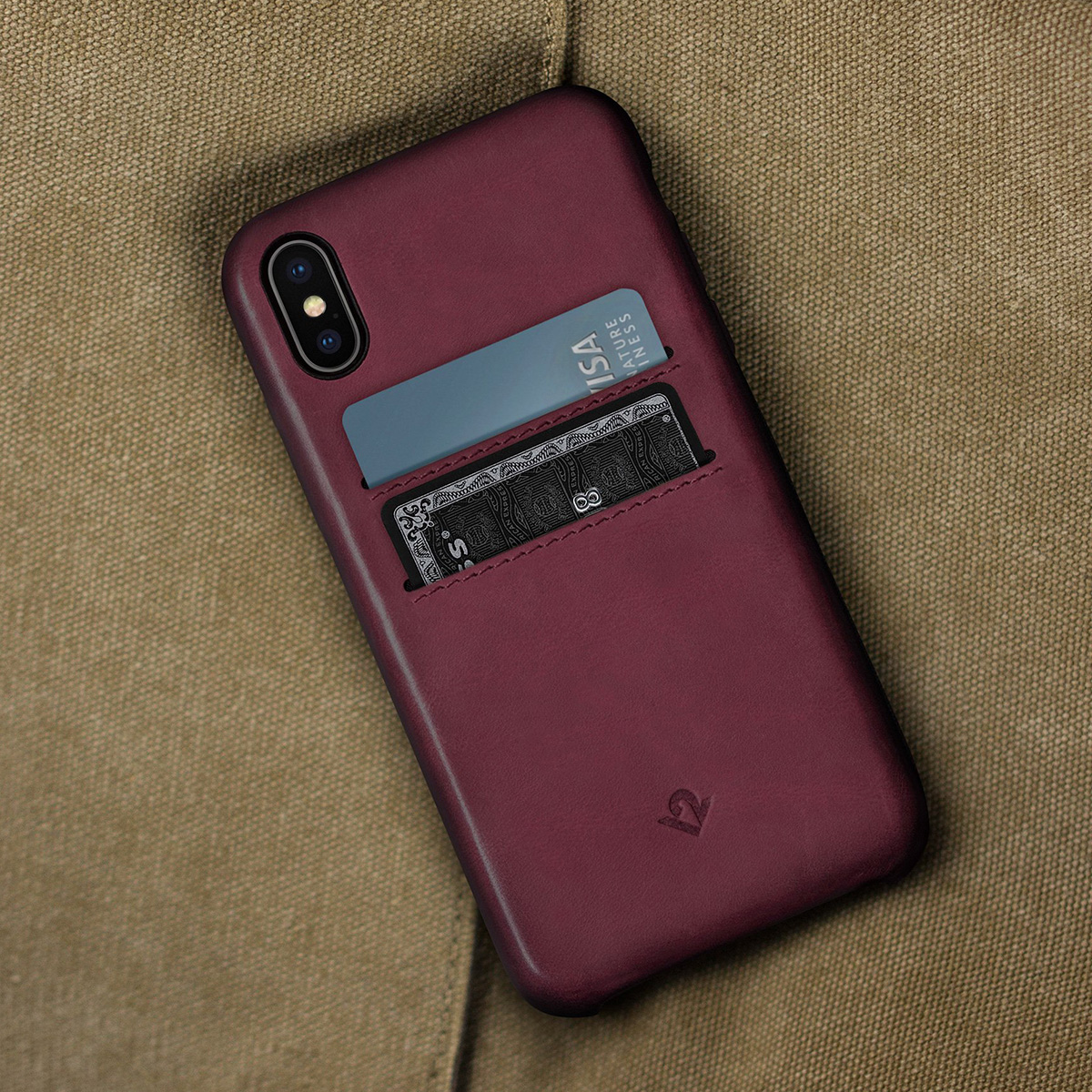 Custodia per telefono bordeaux con fessure per carte, con una carta Visa blu e una nera. Su tessuto marrone.