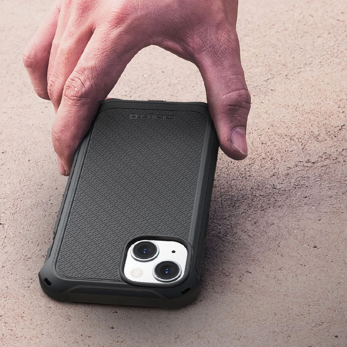 Una mano tiene una custodia nera per telefono. La custodia è su una superficie beige. Il telefono ha un rigonfiamento della fotocamera.