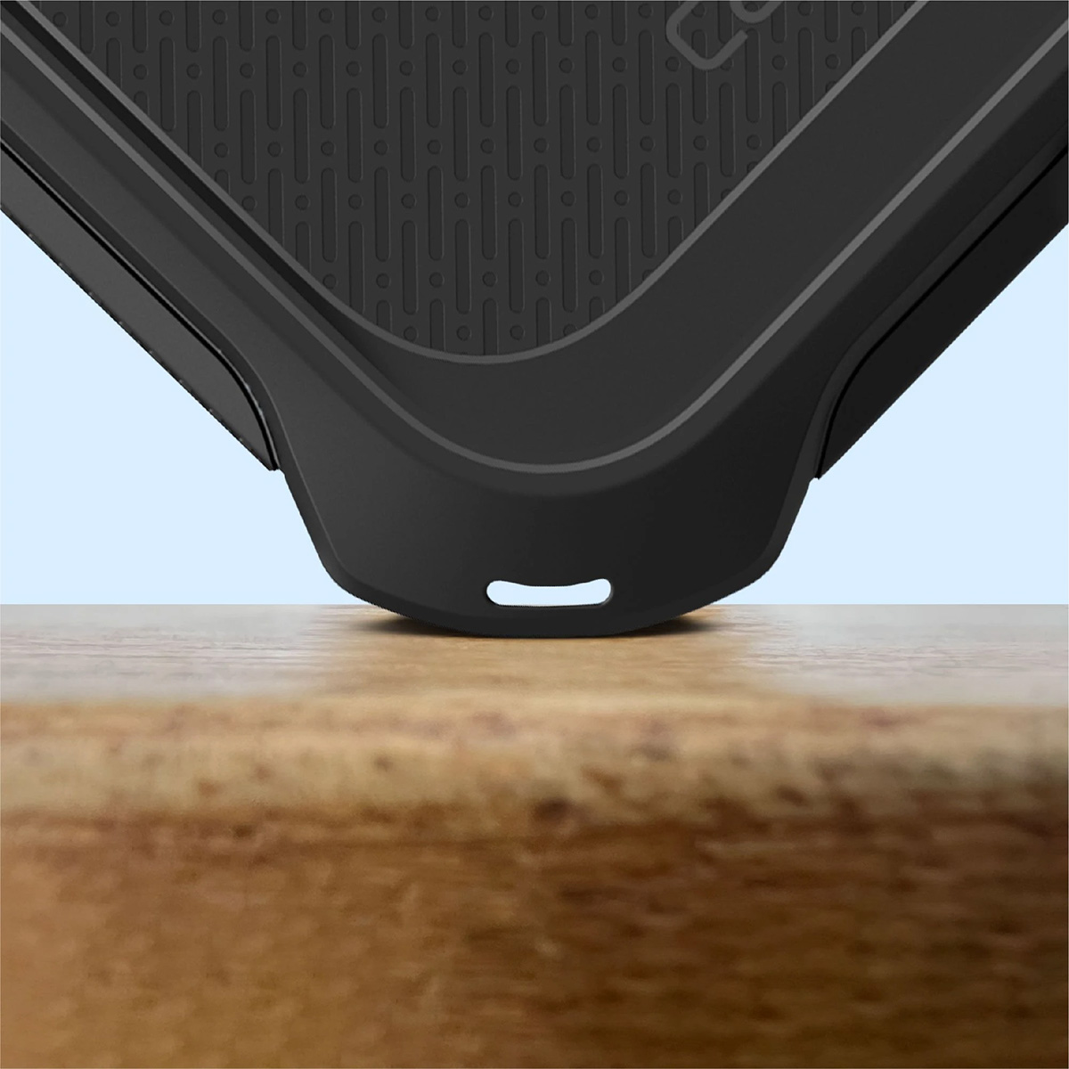 Primo piano di una custodia per telefono nera su una superficie di legno. La custodia ha una parte superiore strutturata e un fondo curvo con un foro.