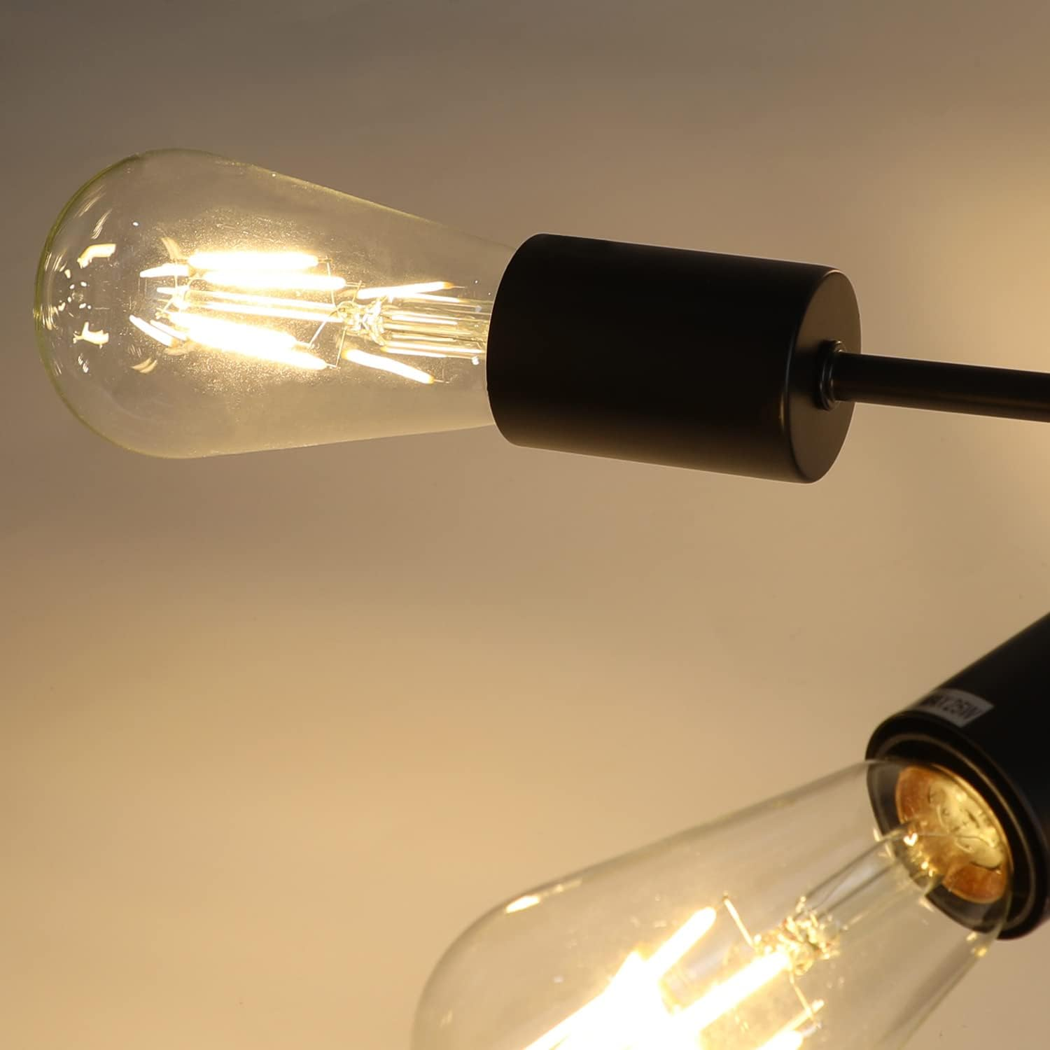 Zbliżenie dwóch zapalonych, przezroczystych żarówek w czarnych oprawach. Tło to gradient od żółtego do beżowego.