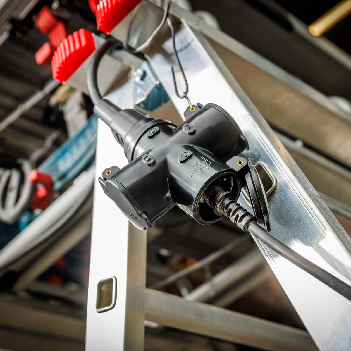 Zwarte stroomverdeler met drie stopcontacten op een metalen ladder. Rode plastic onderdelen zijn zichtbaar.