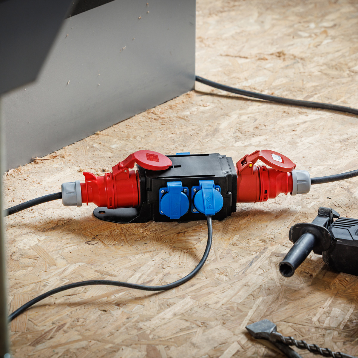 Una scatola di distribuzione di energia nera con connettori rossi e blu è su una superficie di legno. Sono presenti anche cavi neri e un trapano.