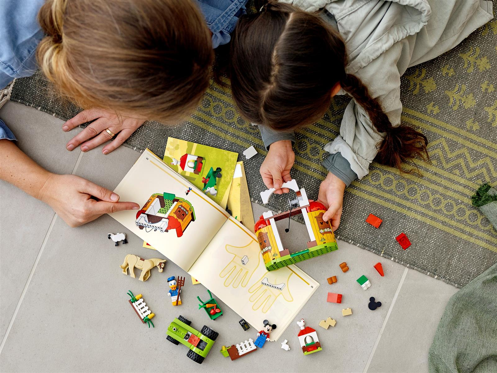 Zwei Personen bauen mit Lego. Ein Buch ist mit Anweisungen geöffnet. Lego-Teile und Figuren sind verstreut.
