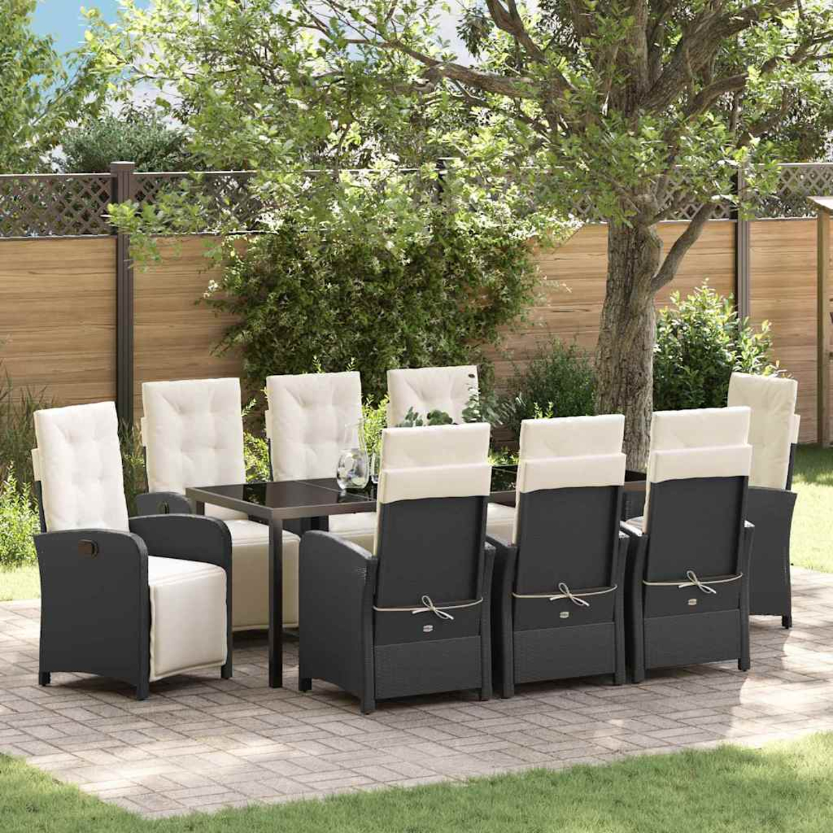Essgruppe im Freien. Schwarze Stühle mit cremefarbenen Kissen um einen dunklen Tisch auf einer Ziegelterrasse. Bäume und ein Zaun im Hintergrund.