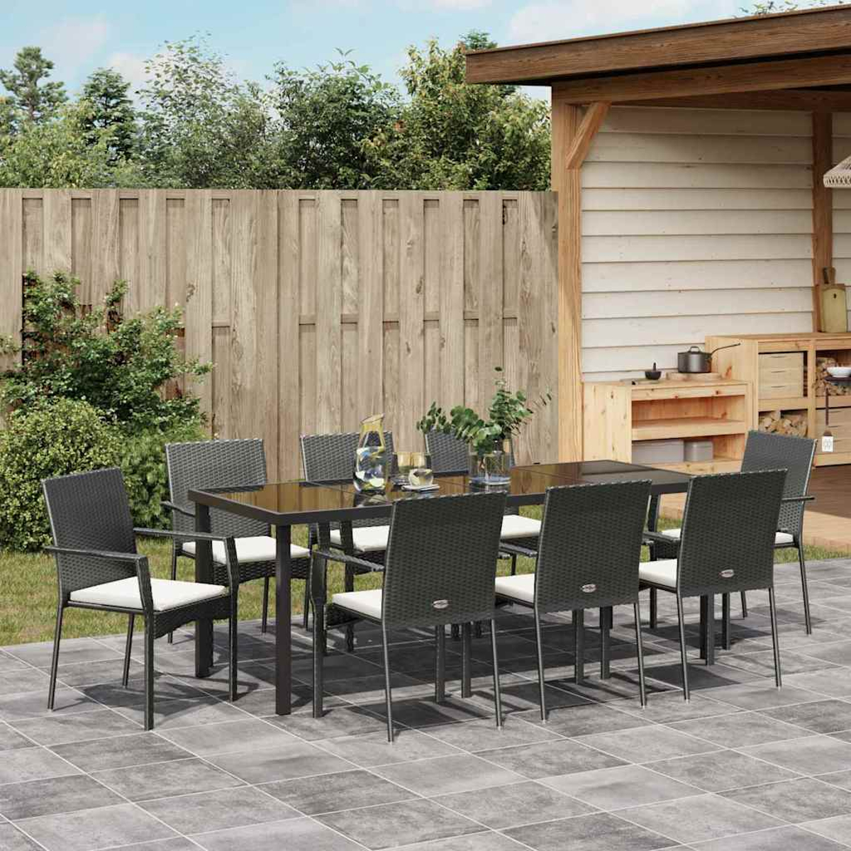Comedor al aire libre con mesa negra y ocho sillas en un patio de baldosas.