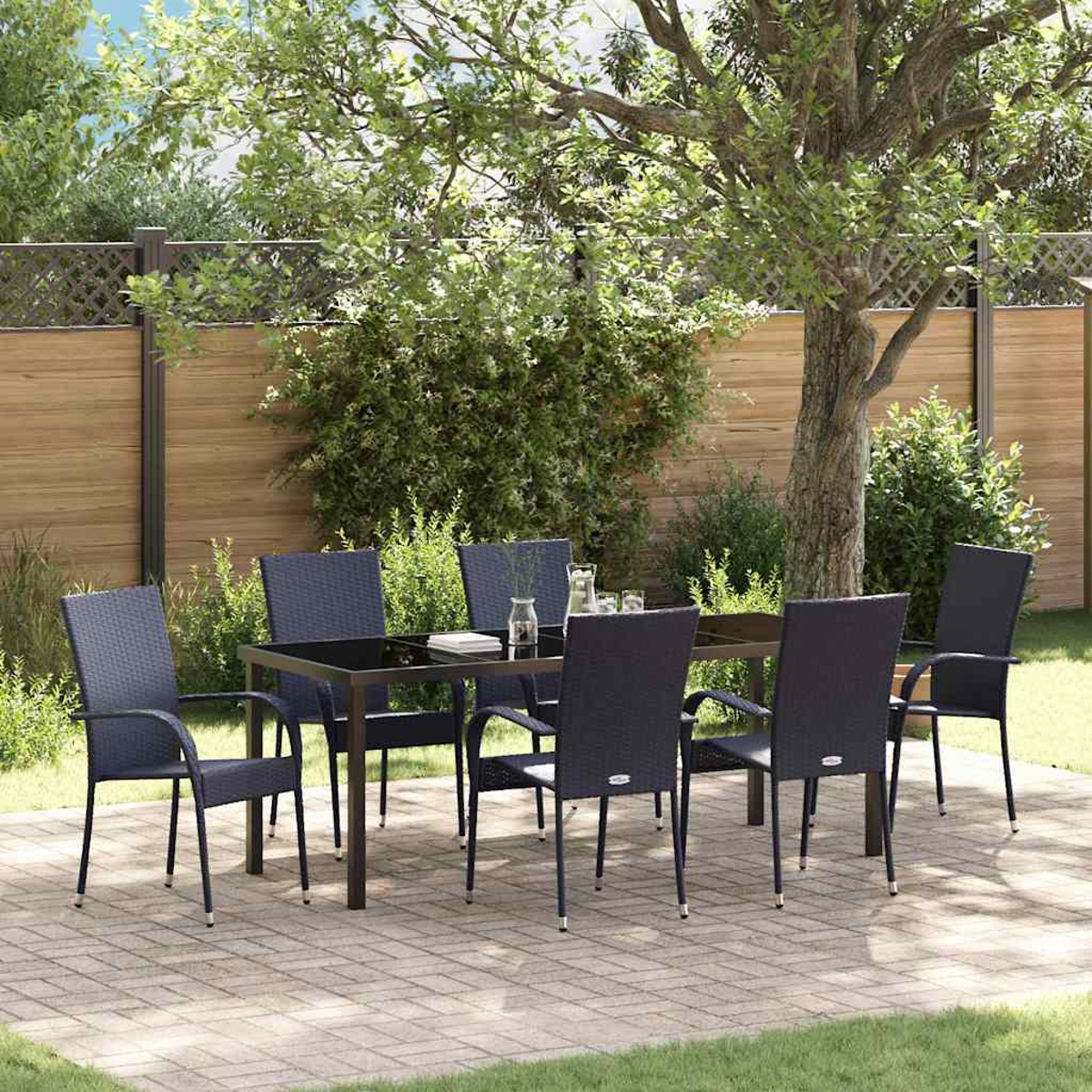 Essgruppe im Freien. Ein schwarzer Tisch und sechs dunkle Stühle stehen auf einer Terrasse. Im Hintergrund ein Holzzaun und ein großer Baum.