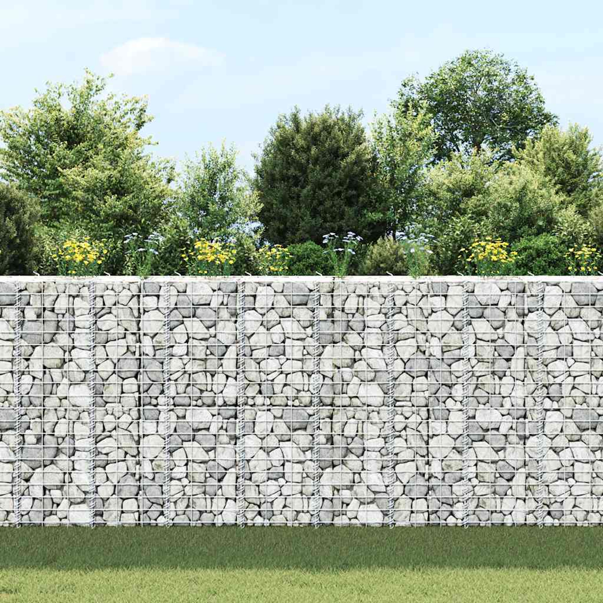 Eine mit grauen Steinen gefüllte Gabionenwand steht vor grünen Bäumen und blauem Himmel.