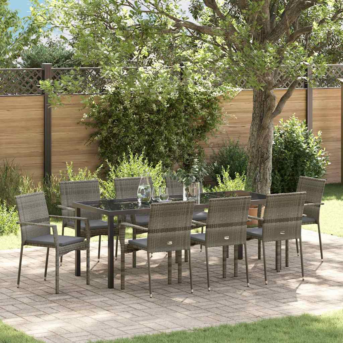 Gartenmöbel-Set mit dunklem Glastisch und acht grauen Korbstühlen auf einer Backsteinterrasse mit grünem Gras.