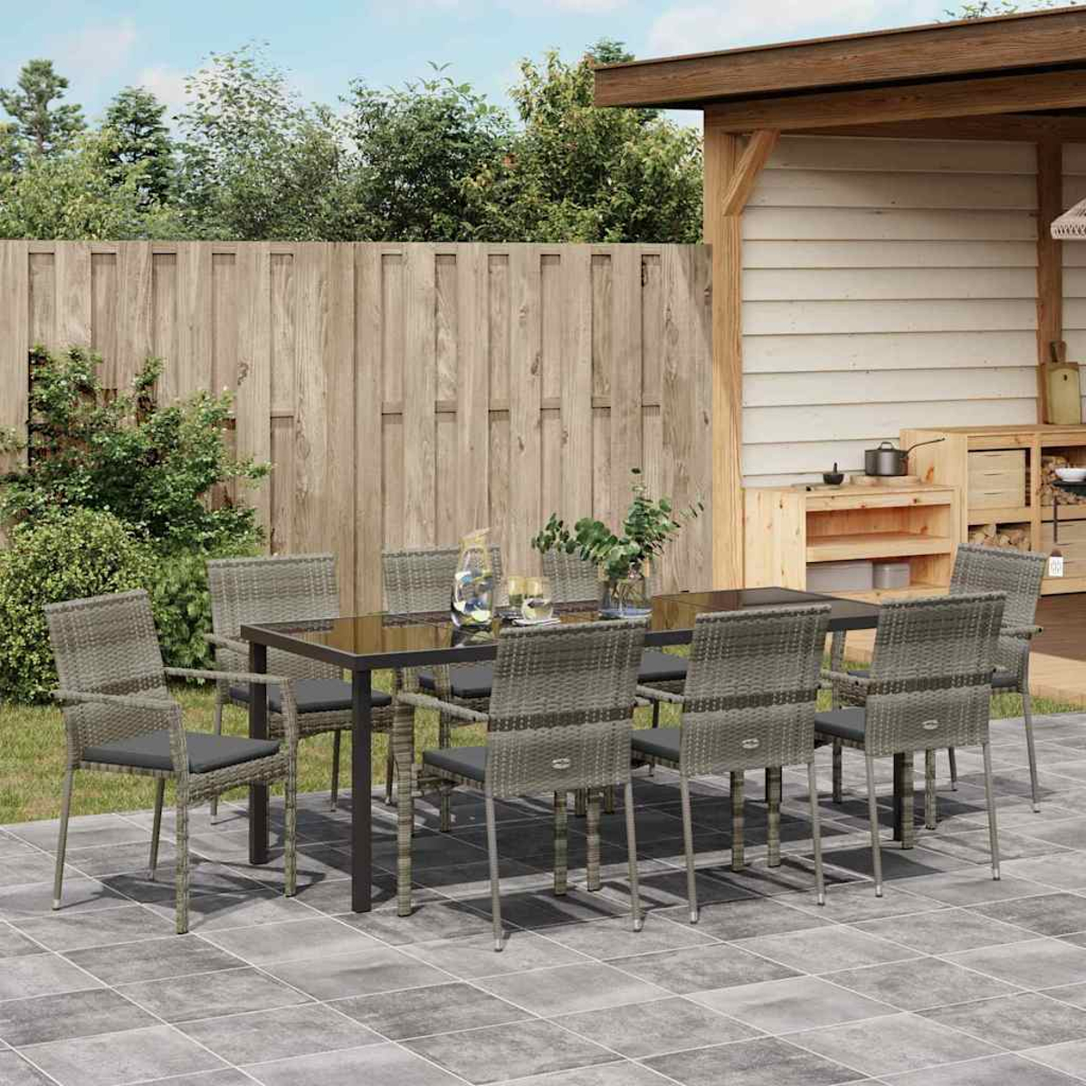 Essgruppe im Freien. Ein schwarzer Tisch mit acht grauen Stühlen. Die Szene spielt sich auf einer Terrasse mit Holzzaun und Holzstruktur ab.