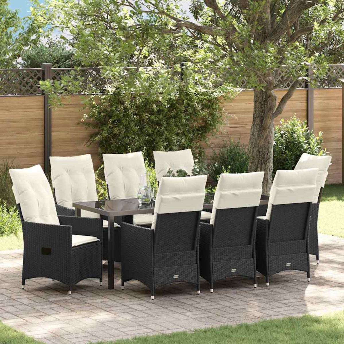Eine Terrassengarnitur mit Tisch und Stühlen. Die Stühle sind aus schwarzem Korbgeflecht mit cremefarbenen Kissen. Die Umgebung ist im Freien mit Holzzaun und Bäumen.