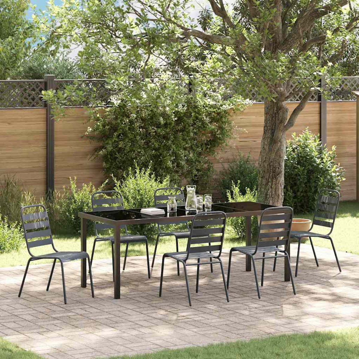 Essgruppe im Freien mit Tisch und Stühlen auf einer Terrasse. Ein Baum beschattet die Szene. Im Hintergrund ein Holzzaun.