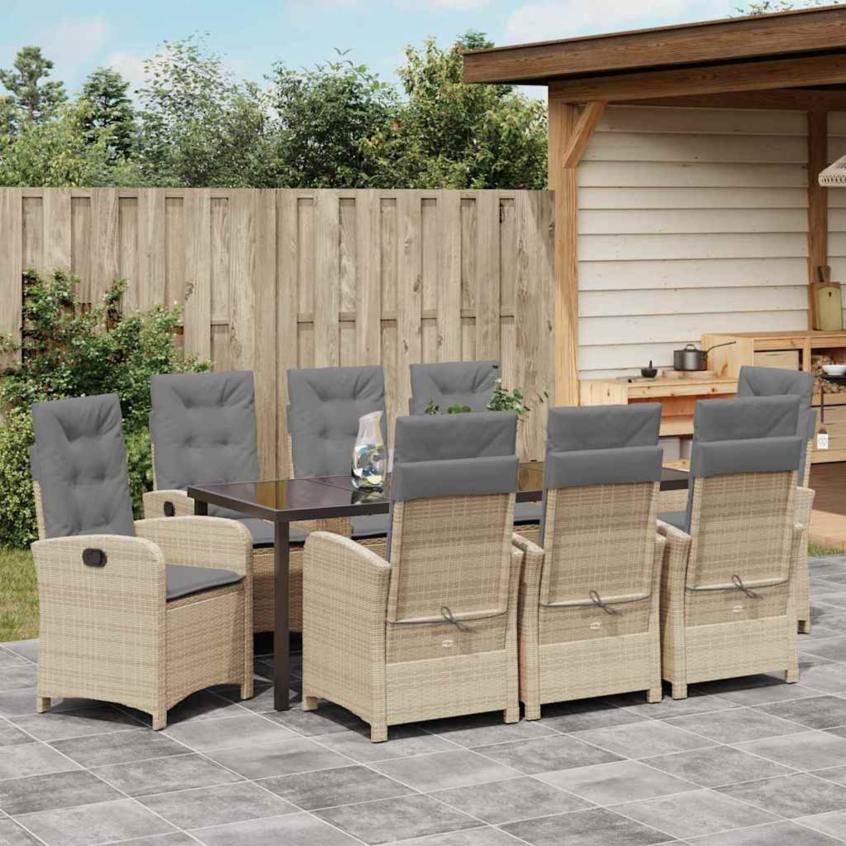 Juego de comedor al aire libre: mesa, sillas con cojines grises, valla de madera, patio. Plantas y estructura de madera al fondo.