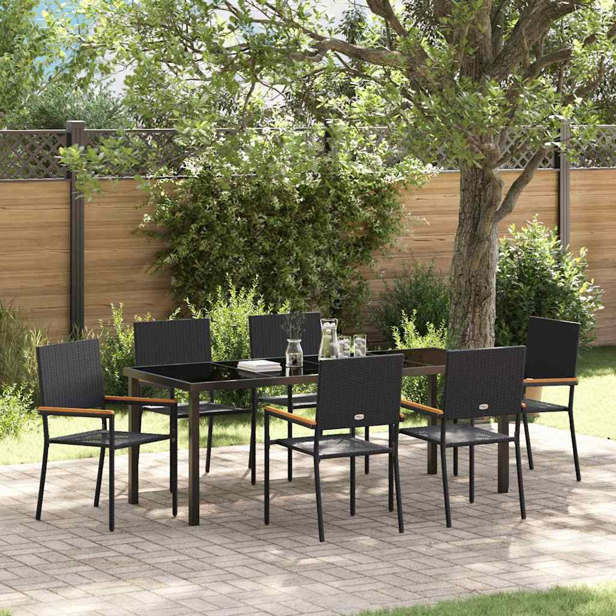 Essgruppe im Freien: ein schwarzer Tisch und Stühle stehen auf einer Terrasse. Im Hintergrund üppiges Grün und ein Holzzaun.
