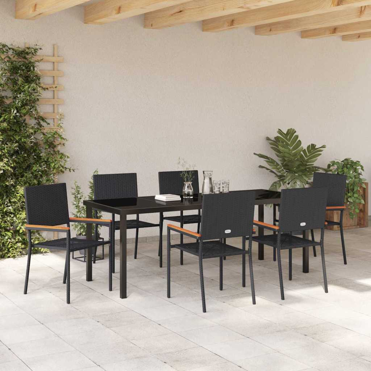 Essgruppe im Freien mit schwarzem Tisch, Stühlen, Pflanzen und einer hellen Wand.