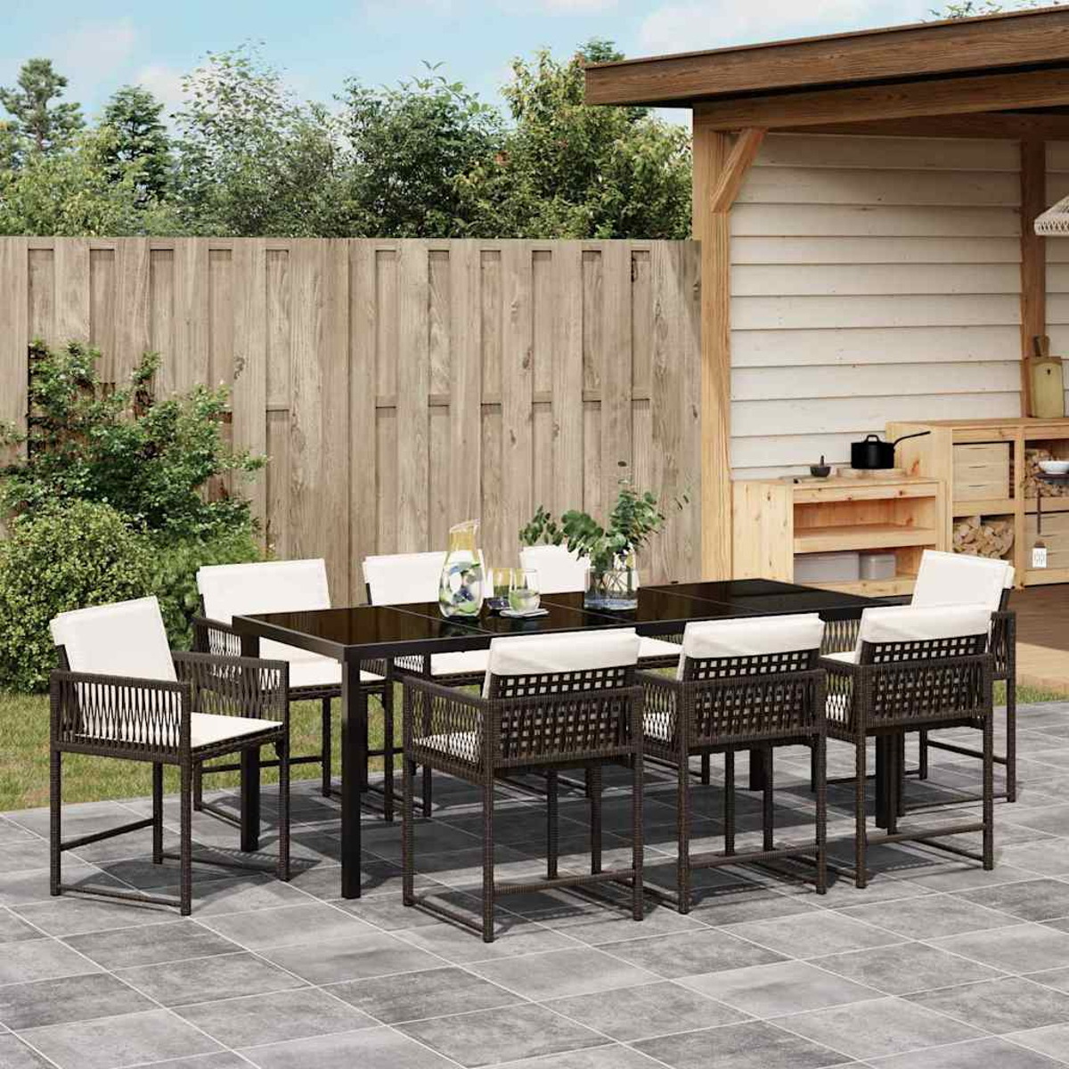 Comedor exterior con mesa oscura y sillas de mimbre con cojines blancos en un patio.