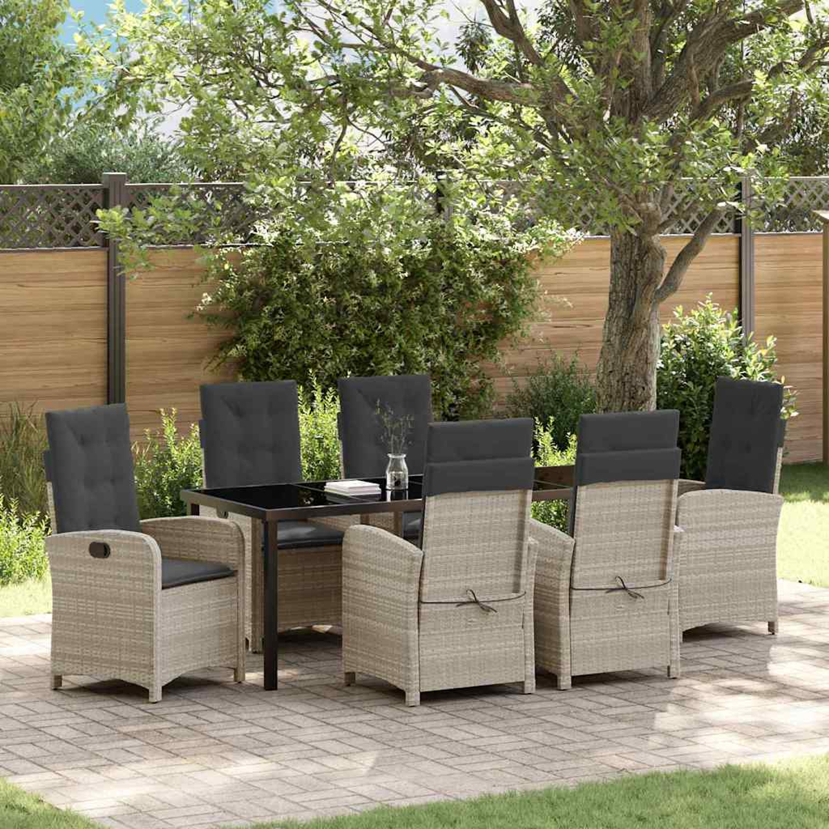 Essgruppe im Freien. Rattan-Stühle mit schwarzen Kissen umgeben einen schwarzen Tisch. Im Hintergrund ein Holzzaun und Grün.