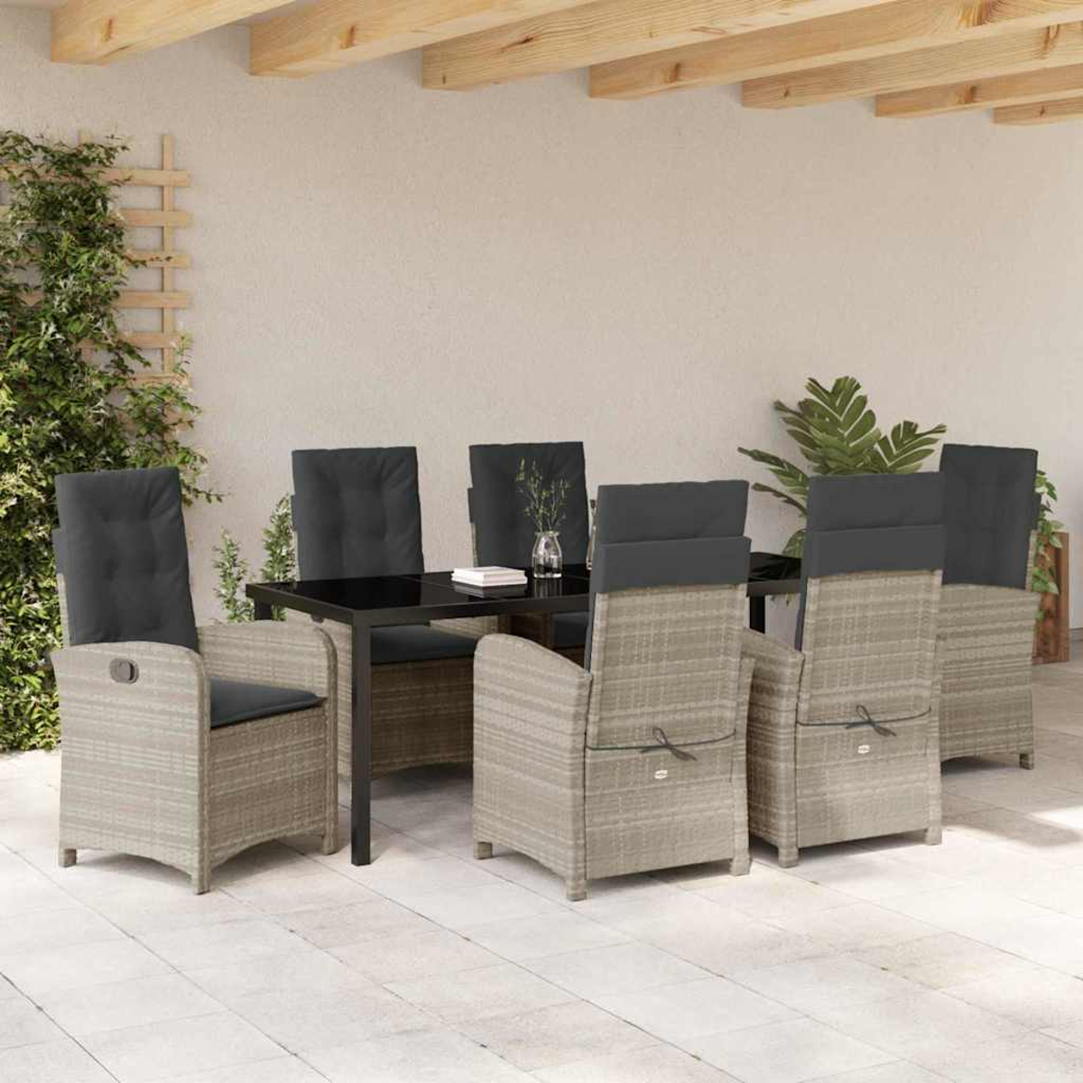 Essgruppe im Freien. Rattanstühle mit grauen Kissen umgeben einen schwarzen Tisch. Grüne Pflanzen im Hintergrund. Beigefarbene Terrasse.